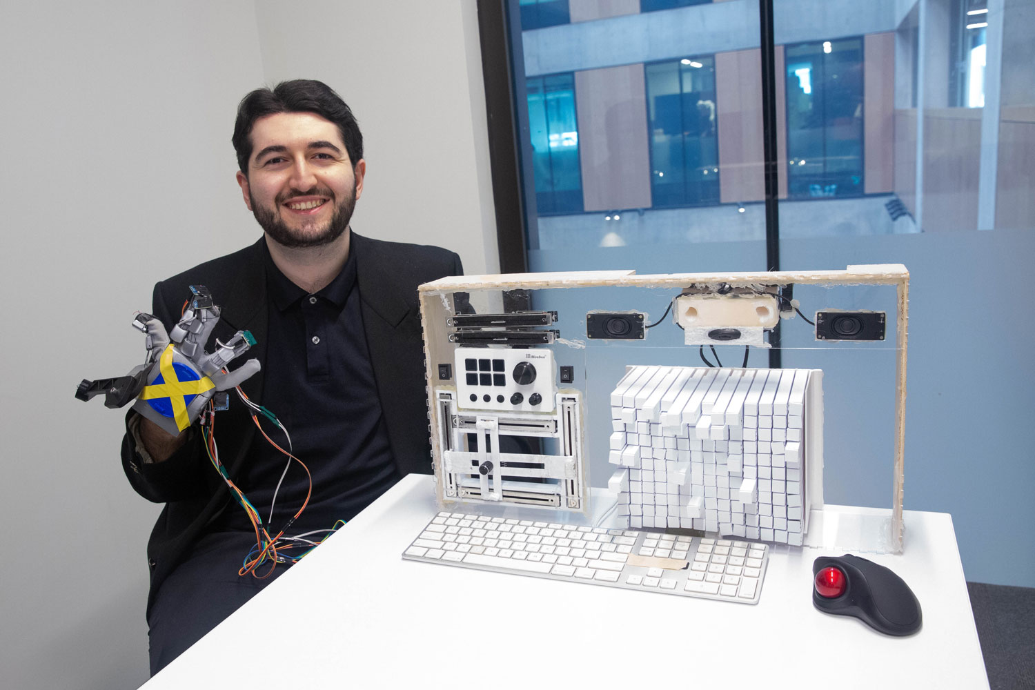 Alex Kurk with a tactile display prototype and modified glove beside a keyboard and trackball.